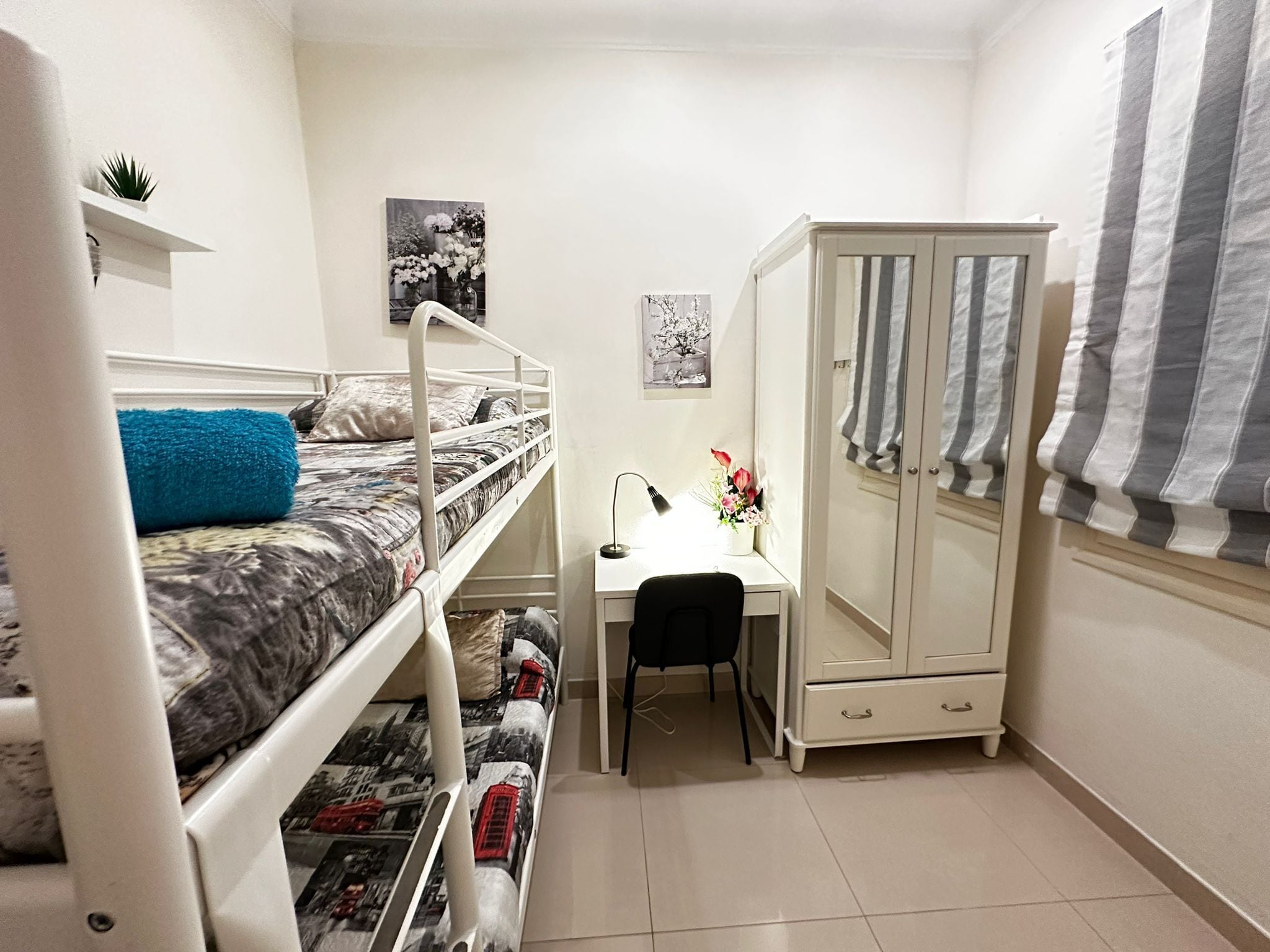 Ein Schlafsaalzimmer mit Etagenbetten, einem Schreibtisch mit Stuhl, einem Kleiderschrank und einer kleinen Pflanze.