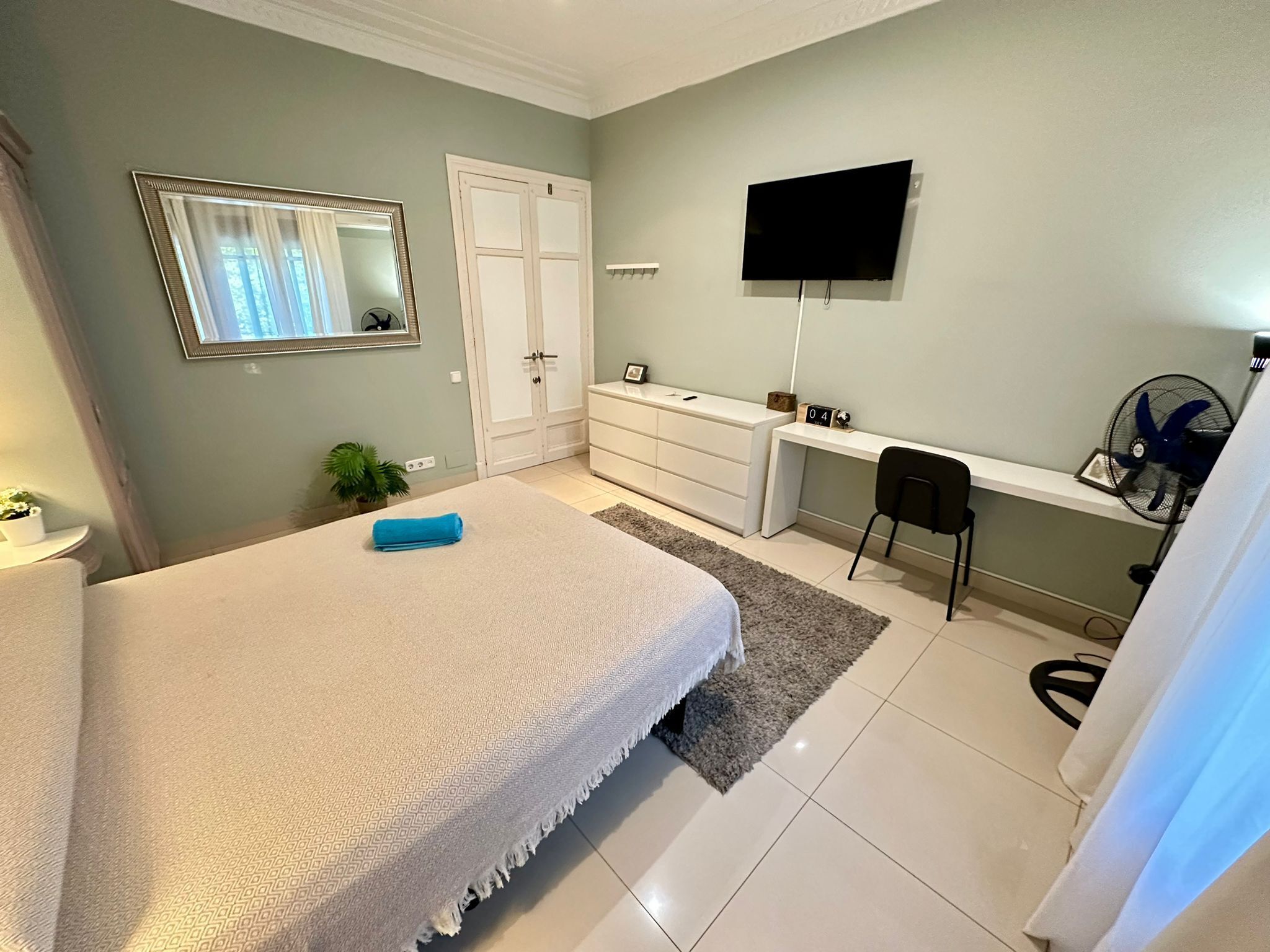 A bedroom with a bed, a desk, a TV, and a chair.
