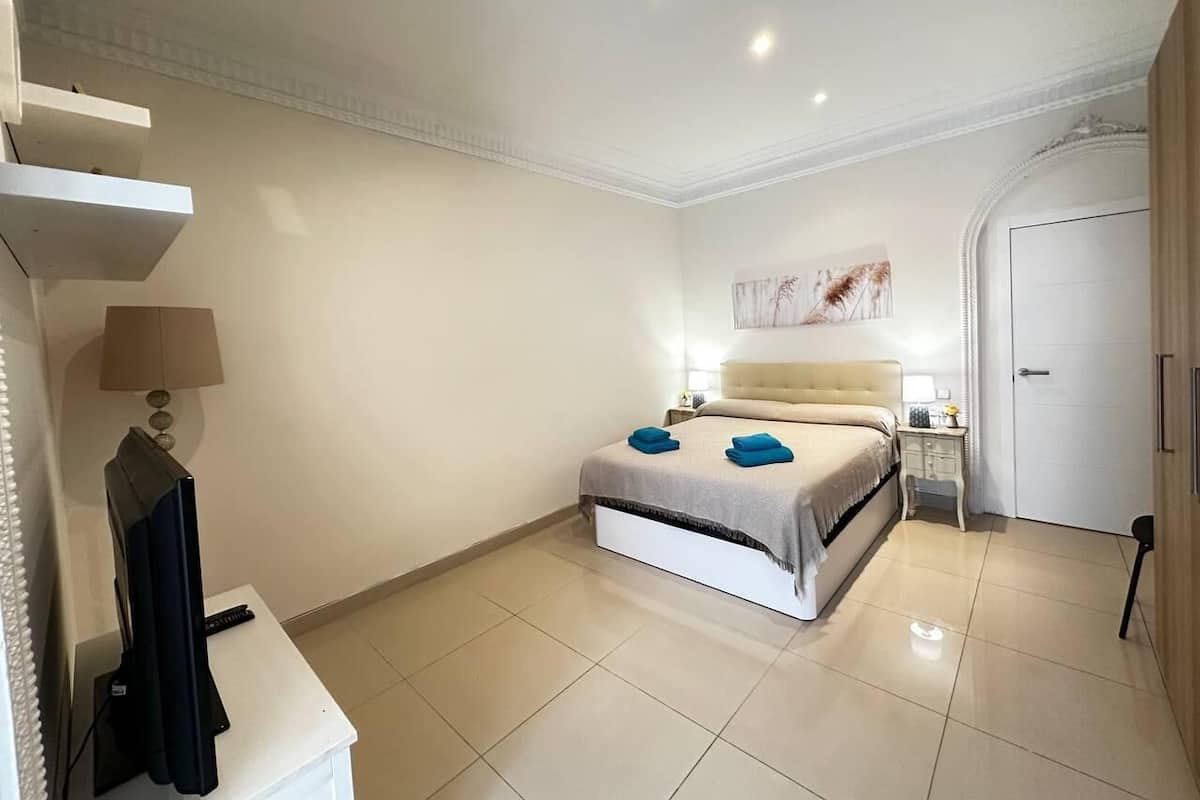 A hotel room with a bed, bedside tables, a TV, and a door.