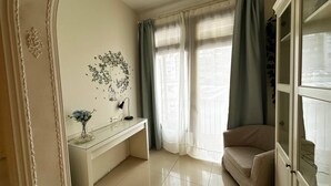 Een goed verlichte kamer met een witte console tafel, een beige fauteuil en een groot raam met dunne gordijnen.
