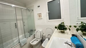 Een moderne badkamer met een douchecabine, toilet, bidet en een grote wastafel met spiegel.