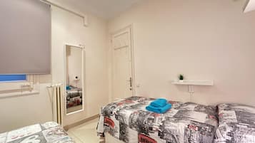 A bedroom with a bed covered in a patterned blanket, a bedside table with a plant, and a mirror on the wall.