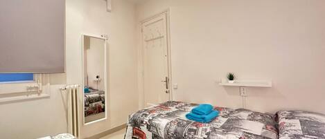 A bedroom with a bed covered in a patterned blanket, a bedside table with a plant, and a mirror on the wall.