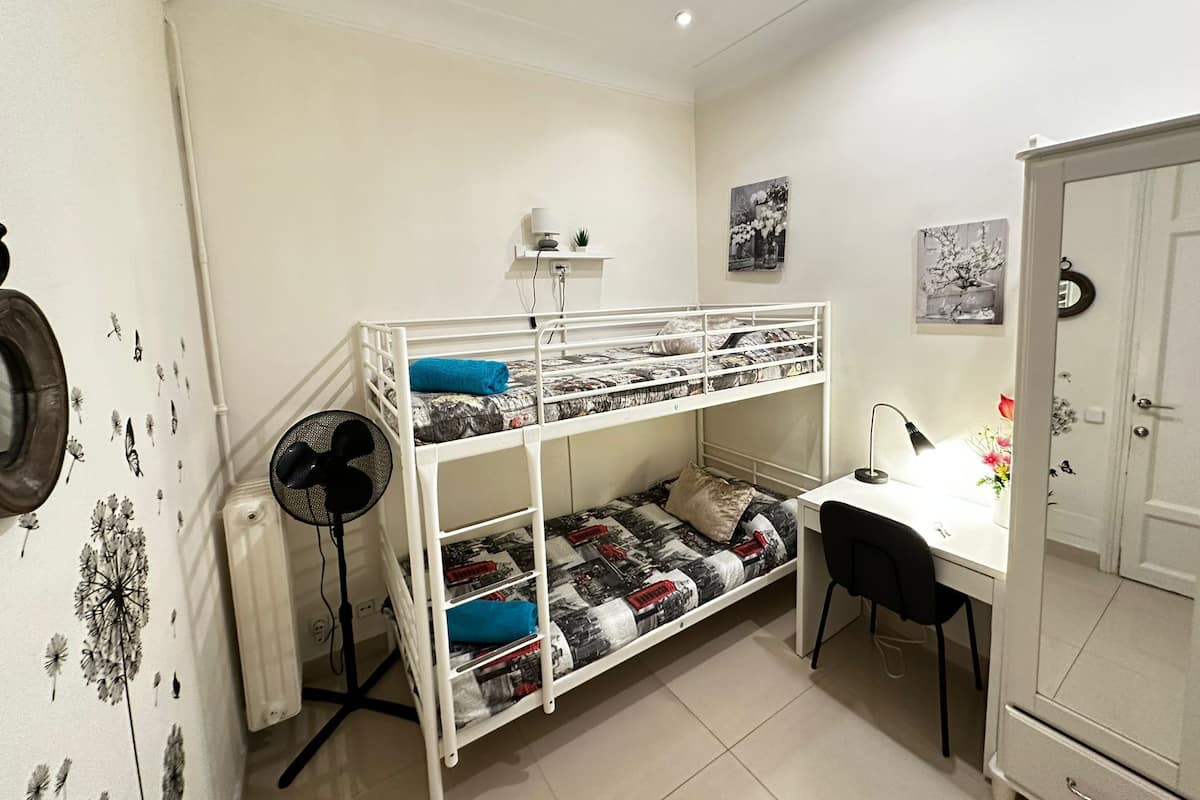 A bunk bed with a desk and chair, a standing fan, and a cabinet.