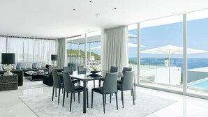 Una sala de estar moderna con comedor, ventanas amplias y vista al océano.
