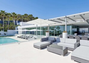 A modern outdoor pool area with lounge chairs and umbrellas, a glass-enclosed dining area, and a clear view of the surrounding landscape. - Stylish Villa Near Ibiza Town (Ibiza Town)