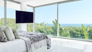Un dormitorio moderno con una cama grande, un televisor de pantalla plana y vistas al océano y la vegetación.