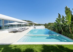 A modern infinity pool with white lounge chairs and umbrellas, surrounded by lush greenery and a clear blue sky. - Stylish Villa Near Ibiza Town (Ibiza Town)