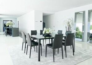A modern dining area with a rectangular table and six chairs, a kitchen in the background, and a large window with a view of greenery. - Stylish Villa Near Ibiza Town (Ibiza Town)
