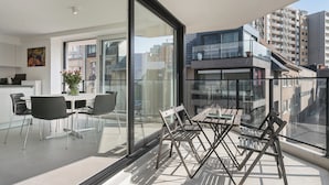 A modern apartment with a balcony, a dining area with chairs and a table, and a kitchen visible through a glass door. - Apartment in Blankenberge Near Beach (Blankenberge)