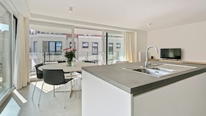 A modern kitchen with a large island, a dining area with a table and chairs, and a TV mounted on the wall. - Apartment in Blankenberge Near Beach (Blankenberge)