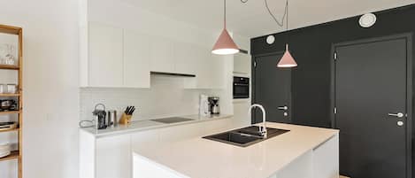 Een moderne keuken met witte kastjes, een centraal kookeiland met spoelbak en hanglampen.