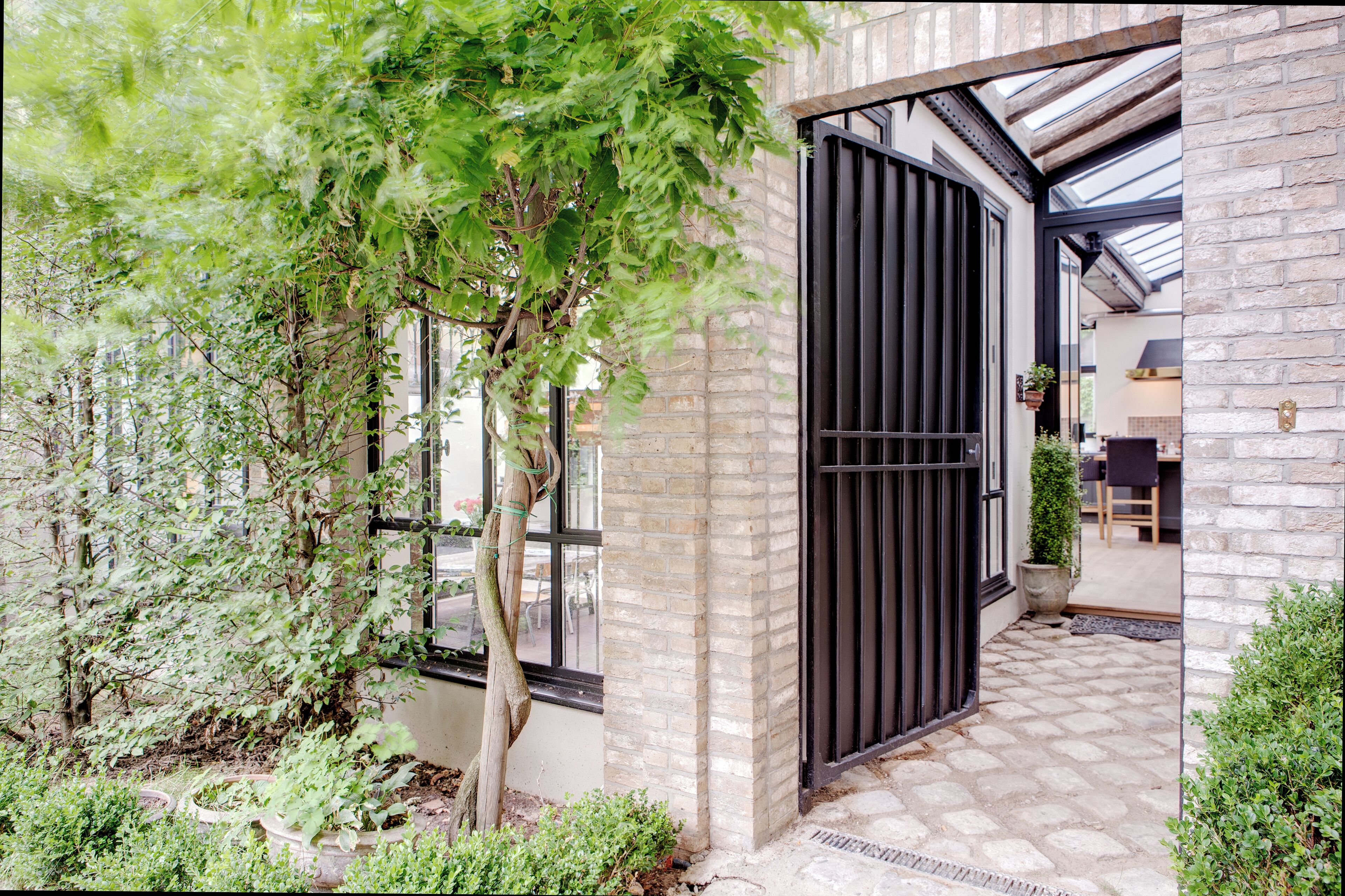 Een modern gebouw met een bakstenen gevel, een zwart metalen hek en een tuin met verschillende planten.