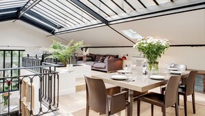 A modern dining area with a high ceiling, a dining table set for four, and a view of the outdoors. - Paris Green House Residence (Paris)