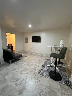 Quarto com televisão de tela plana na parede, uma mesinha com cadeira e um sofá.