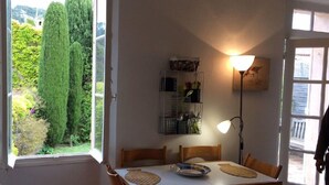 Un coin repas comprenant une table, des chaises, une lampe et une fenêtre donnant sur un paysage verdoyant.