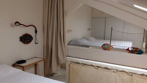 Une chambre avec un lit superposé, une petite table, un rideau et un objet fixé au mur.