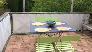 Une terrasse avec une table et des chaises, entourée d’une clôture blanche et de verdure.
