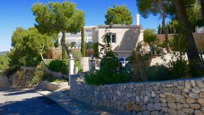 A two-story house with a stone wall and trees in the foreground. - Villa With Golf-course Views (Santa Eulalia del Rio)