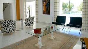 A spacious living room with a glass coffee table, two armchairs, a sofa, and a painting on the wall. - Villa With Golf-course Views (Santa Eulalia del Rio)