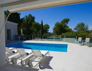 A modern outdoor swimming pool with a clear view of the sea, surrounded by white lounge chairs and a glass-enclosed deck. - Villa With Golf-course Views (Santa Eulalia del Rio)