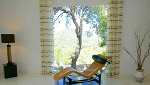 A room with a glass coffee table, a lounge chair, a lamp, and a view of a tree through the window. - Villa With Golf-course Views (Santa Eulalia del Rio)