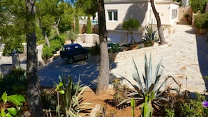 A residential area with a stone pathway, a parked car, and various trees and plants. - Villa With Golf-course Views (Santa Eulalia del Rio)