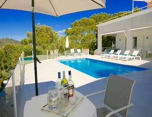 A poolside area with a clear view of the pool, lounge chairs, and a table with bottles and glasses. - Villa With Golf-course Views (Santa Eulalia del Rio)