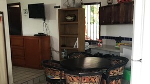 Ein Essbereich mit einem runden Tisch und vier Stühlen, eine Küche mit Holzschränken, einem Fernseher und einem Fenster mit Vorhängen.