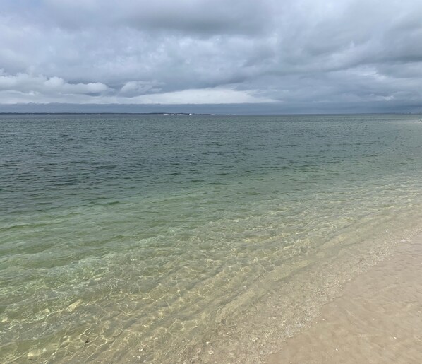 A beach with clear shallow waters and a distant shoreline.