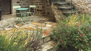 A stone building with a staircase leading to a balcony. There is a table and chairs outside. - La chambre du poete (vernon)
