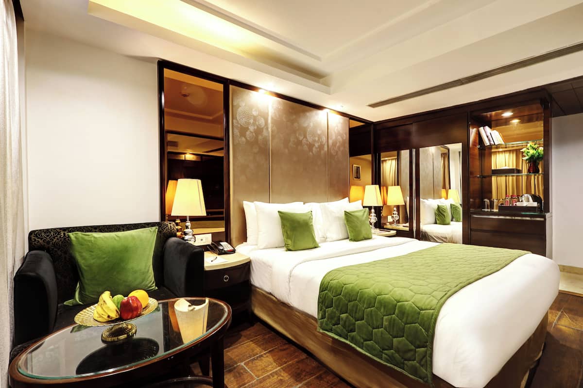 A hotel room with a bed, a sitting area with a table, a nightstand, and a mirror.