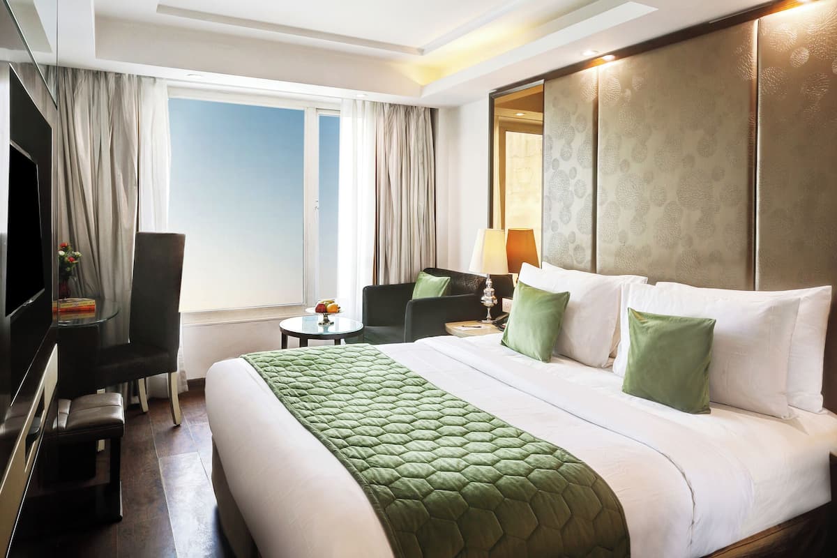 A hotel room with a large bed, a desk, a chair, a TV, and a window with curtains.