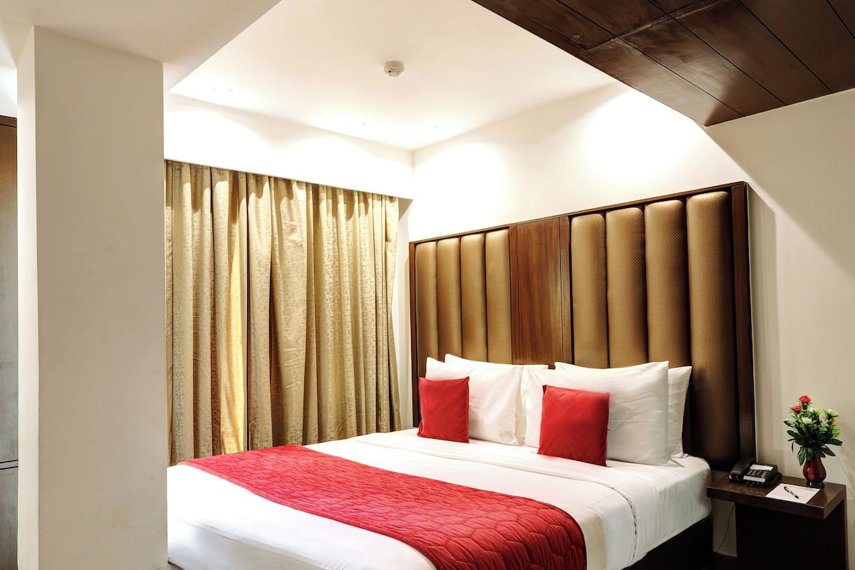A hotel room with a large bed, wooden headboard, and a nightstand with a phone and a vase.