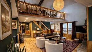 A spacious living area with a staircase leading to an upper level, a fireplace, and a television. - Easy Access •Mtn View• Hot Tub• Pool• Game Room• Porch• Wildlife•Minutes to Town (Ellijay)