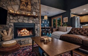 A cozy living room with a stone fireplace, leather sofa, and a dining area visible through an open doorway. - Easy Access •Mtn View• Hot Tub• Pool• Game Room• Porch• Wildlife•Minutes to Town (Ellijay)