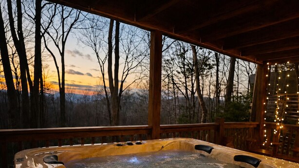 A hot tub with a digital control panel, surrounded by a wooden deck with a view of trees and a sunset. - Easy Access •Mtn View• Hot Tub• Pool• Game Room• Porch• Wildlife•Minutes to Town (Ellijay)