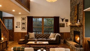A cozy living room with a fireplace, wooden floors, a high ceiling, and a staircase. - Easy Access •Mtn View• Hot Tub• Pool• Game Room• Porch• Wildlife•Minutes to Town (Ellijay)