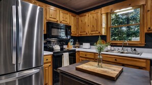 A kitchen with stainless steel appliances, wooden cabinets, and a window with a view of greenery. - Easy Access •Mtn View• Hot Tub• Pool• Game Room• Porch• Wildlife•Minutes to Town (Ellijay)