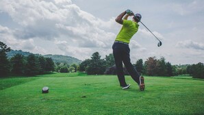 Une personne jouant au golf sur un terrain verdoyant bien entretenu, avec des arbres en arrière-plan.