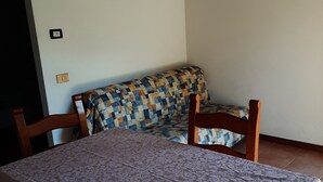 Ein Essbereich mit Tisch für zwei Personen, einer gemusterten Couch, Holzstühlen und einem Fliesenboden.
