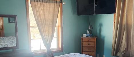 A bedroom with a bed, a ceiling fan, a TV, and a window with curtains.