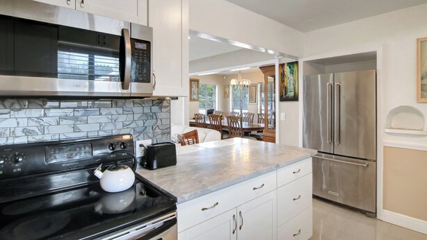 A modern kitchen with white cabinets, a stainless steel refrigerator, a black stove, and a marble countertop.