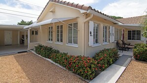 A two-story house with a tiled roof, a covered porch, and a well-maintained garden with red flowers.