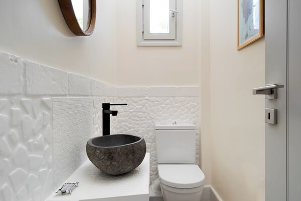 Un baño moderno con lavamanos de piedra, un inodoro blanco y una ventana pequeña.