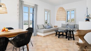 Uma sala de estar moderna com sofá, mesa de jantar e cadeiras, janelas amplas e luminária pendente.