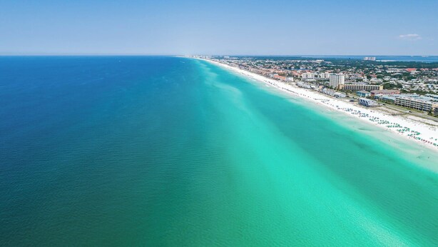 An aerial view of a coastal area with a beach, buildings, and a clear blue sea. - Private Community Beach - Pool - Gated Community (Destin)