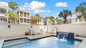 A swimming pool with a waterfall feature, surrounded by palm trees and white lounge chairs. - Private Community Beach - Pool - Gated Community (Destin)