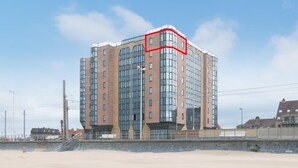 A multi-story hotel with a modern architectural design, featuring large windows and a prominent corner section highlighted in red. - Apartment With sea View Near Raversijde (Ostend)