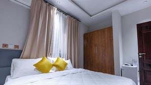 A bedroom with a bed, curtains, a wardrobe, and a door. - Capital 11 Hotel (North Legon)